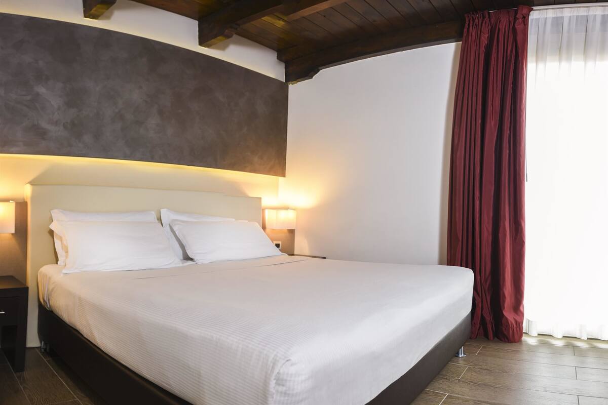 A neatly made bed with white linens, a wooden headboard, and two bedside lamps.