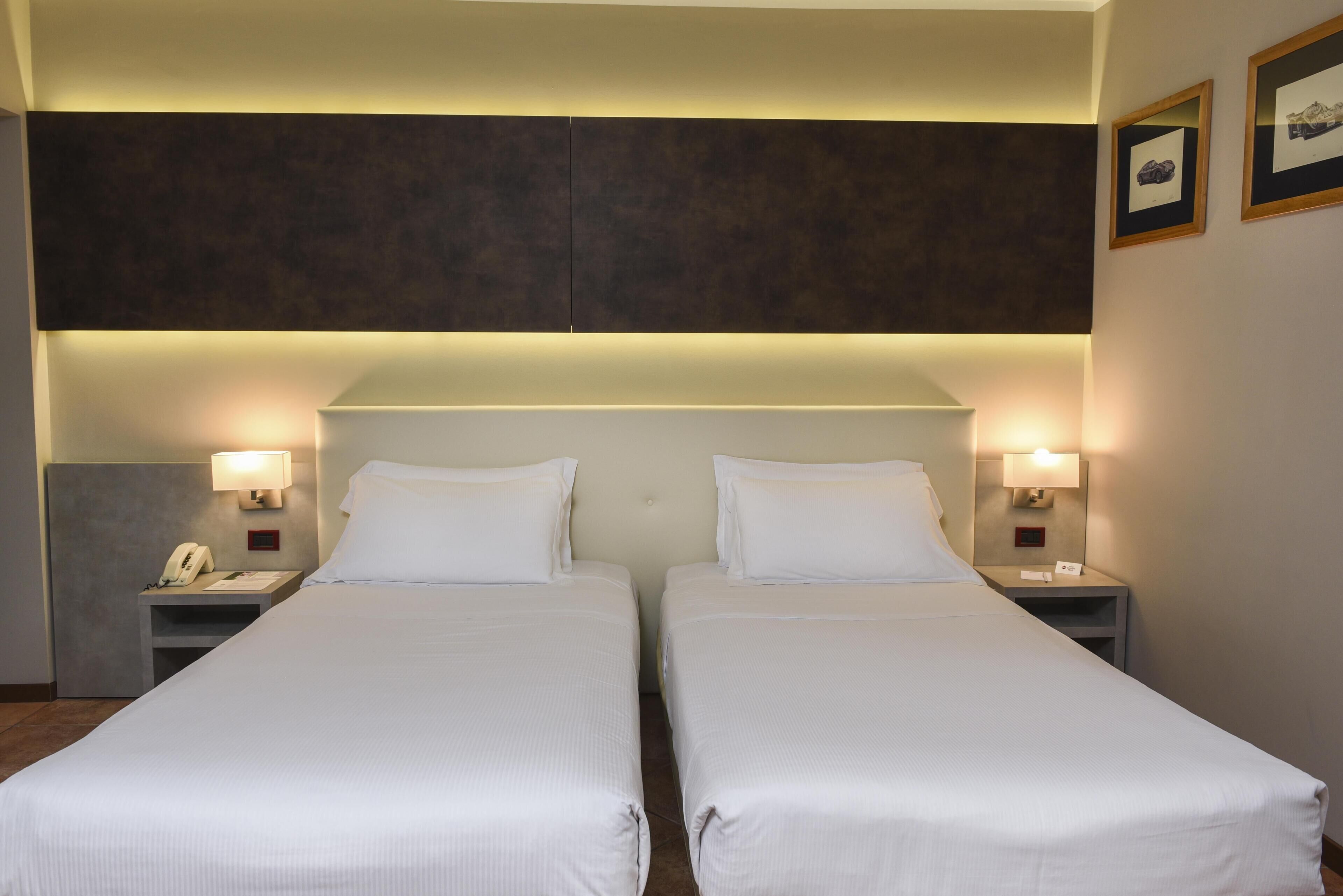 Una habitación de hotel con dos camas individuales, mesitas de noche con lámparas, un teléfono y cuadros en la pared.