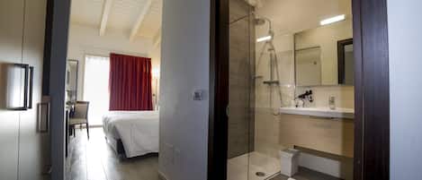 A hotel room with a bed, a desk, a shower, and a bathroom with a mirror and sink.