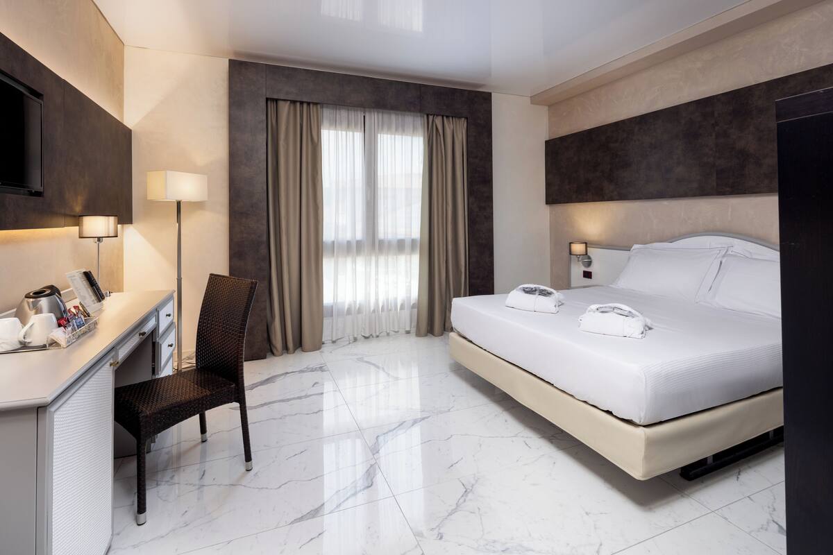 A hotel room with a bed, desk, chair, and a TV mounted on the wall.