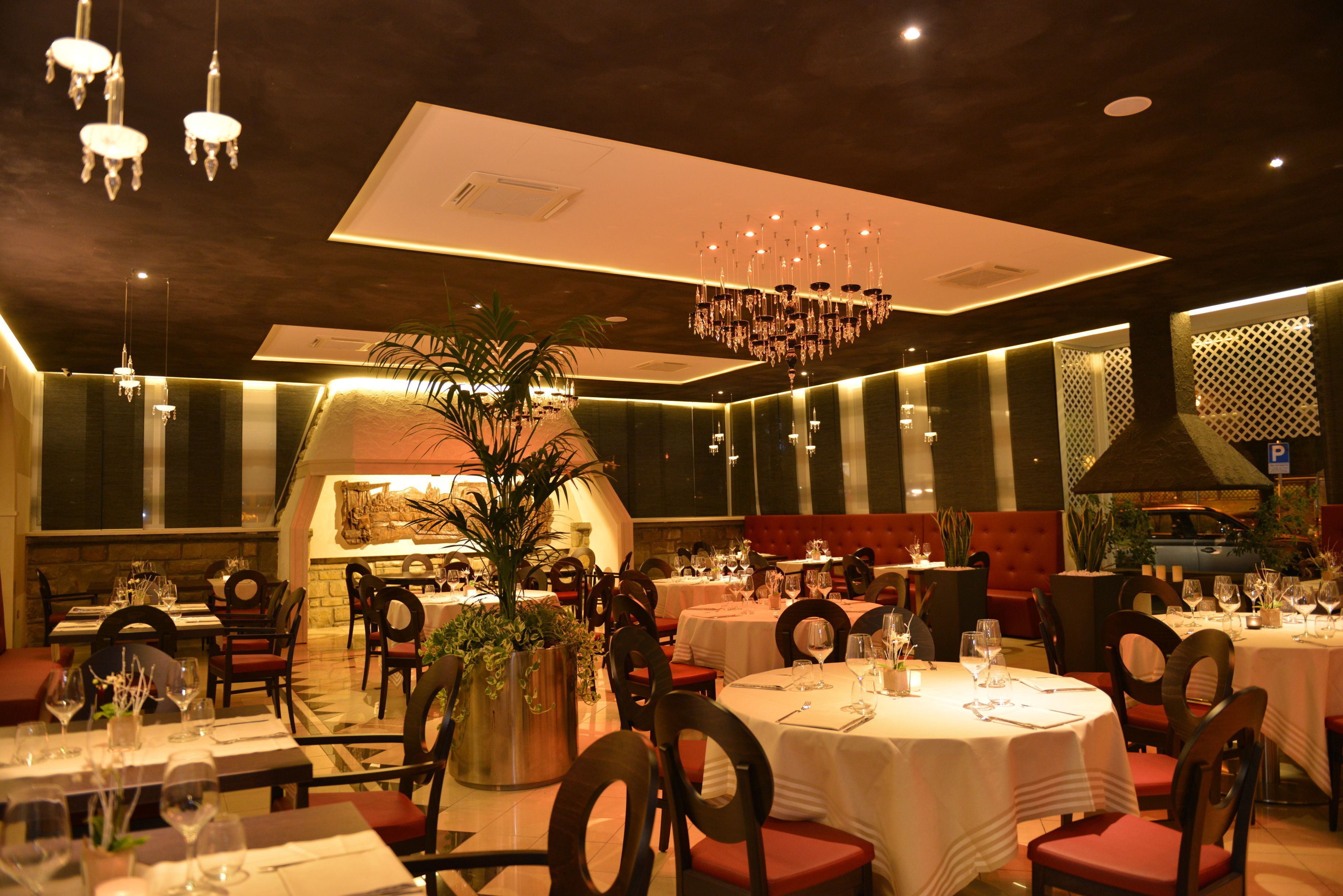 Ein Restaurant mit runden Tischen, roten Sitzgelegenheiten und einem zentralen Kronleuchter.