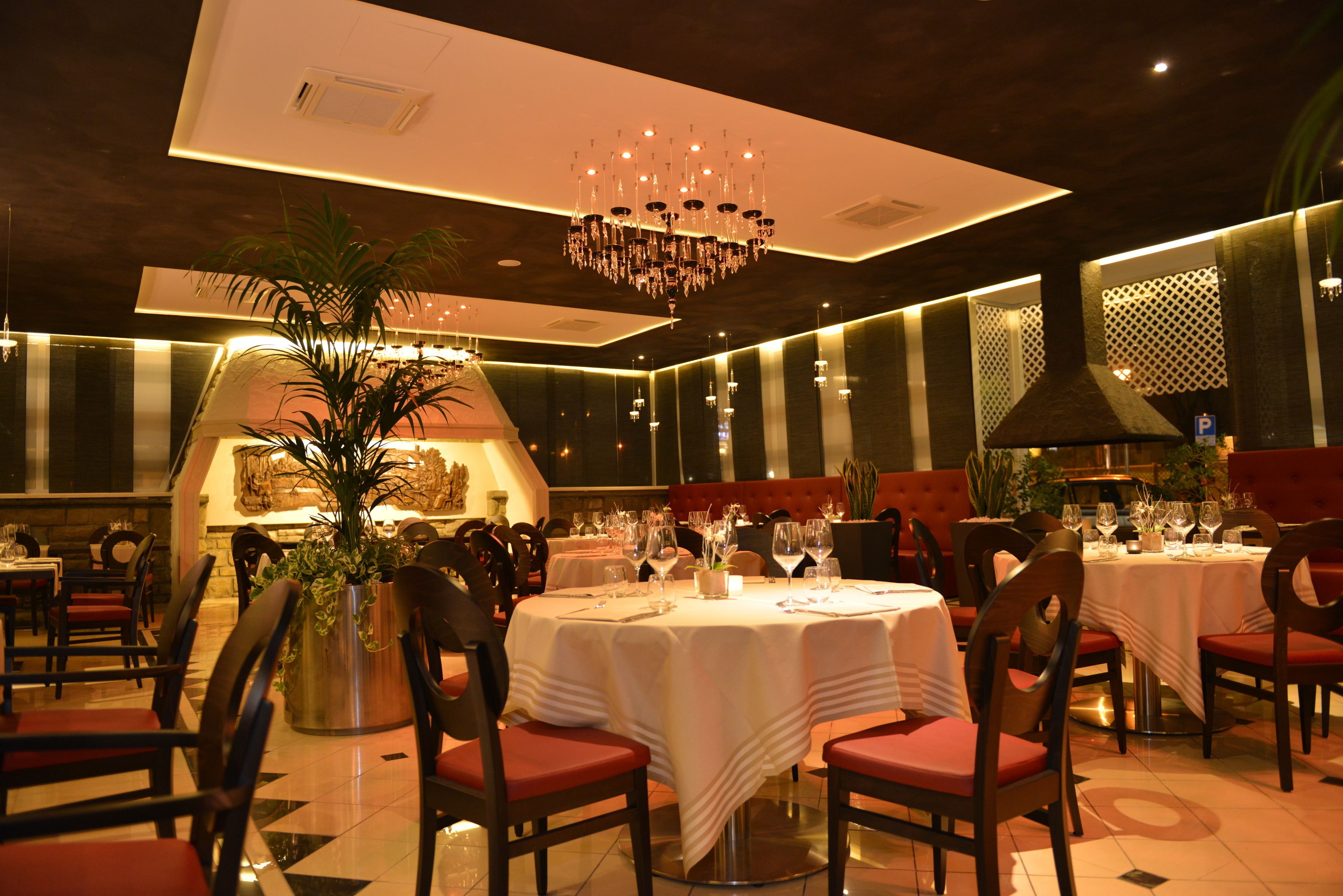 A restaurant with round tables, red chairs, and a chandelier.