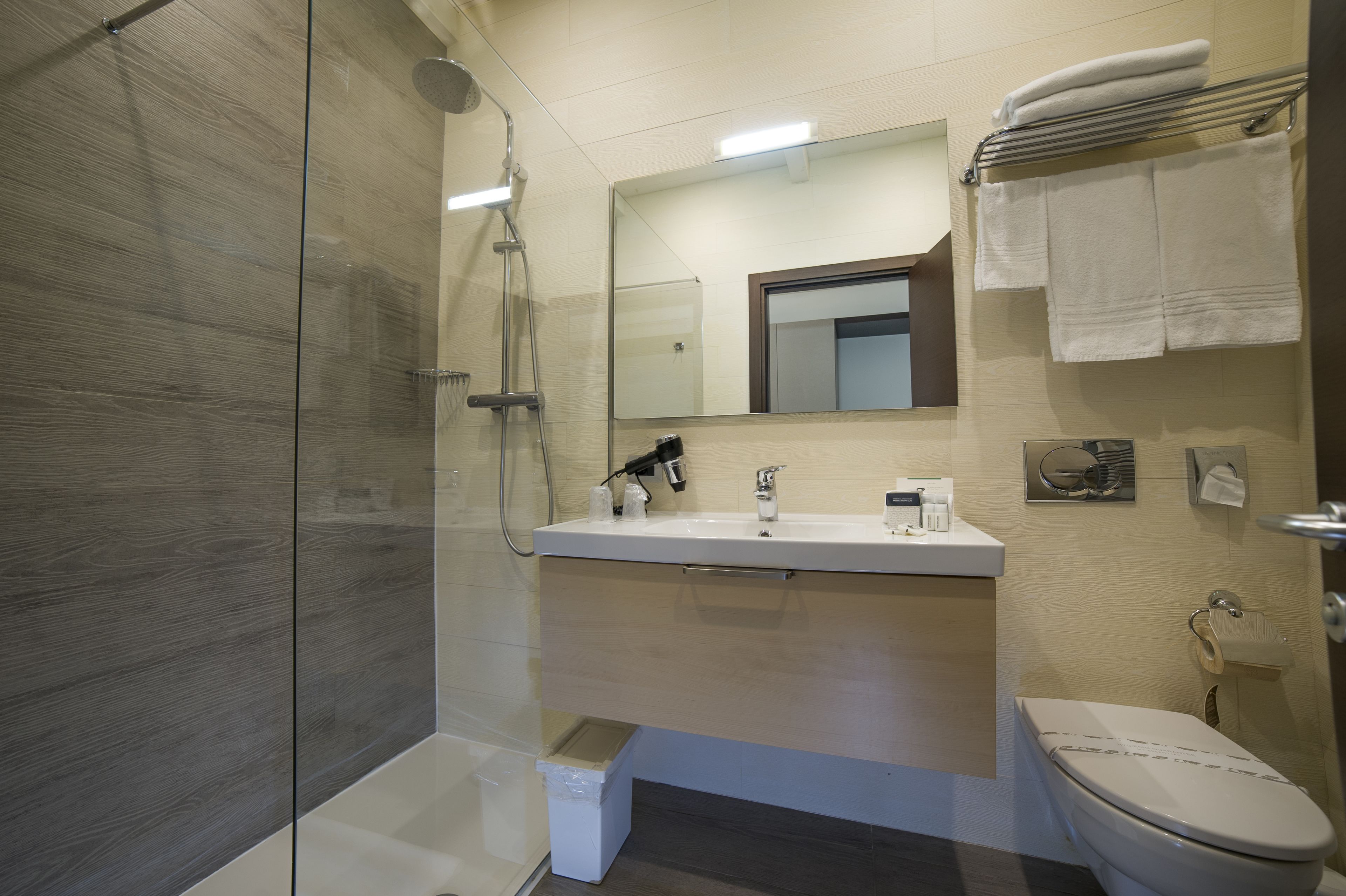 A modern bathroom with a glass shower enclosure, a white sink with a mirror above, and a toilet with a towel rack above it.