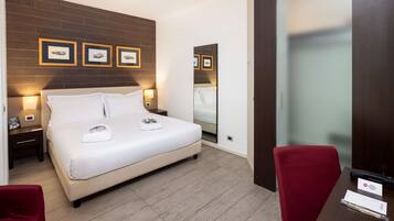 A hotel room with a bed, two bedside tables, a mirror, a red chair, and a wooden floor.
