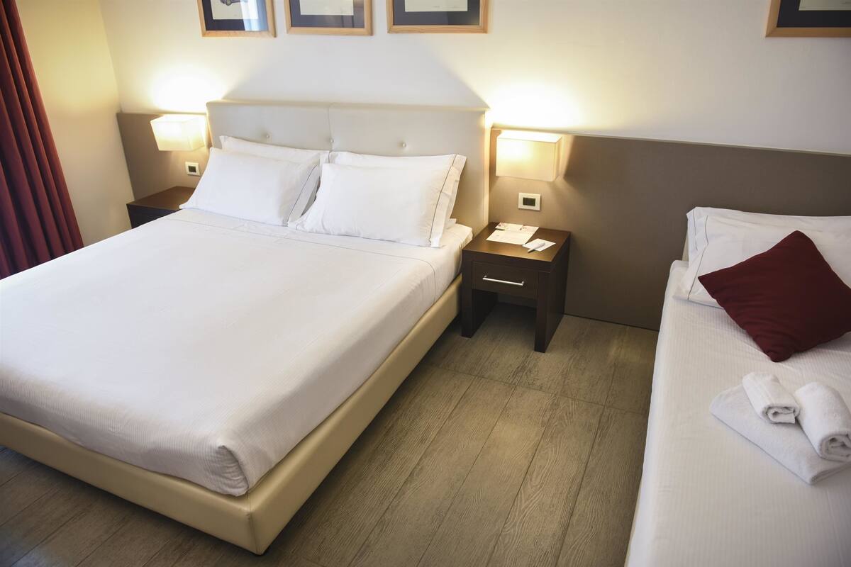 A hotel room with a large bed, two bedside tables, and a smaller bed.