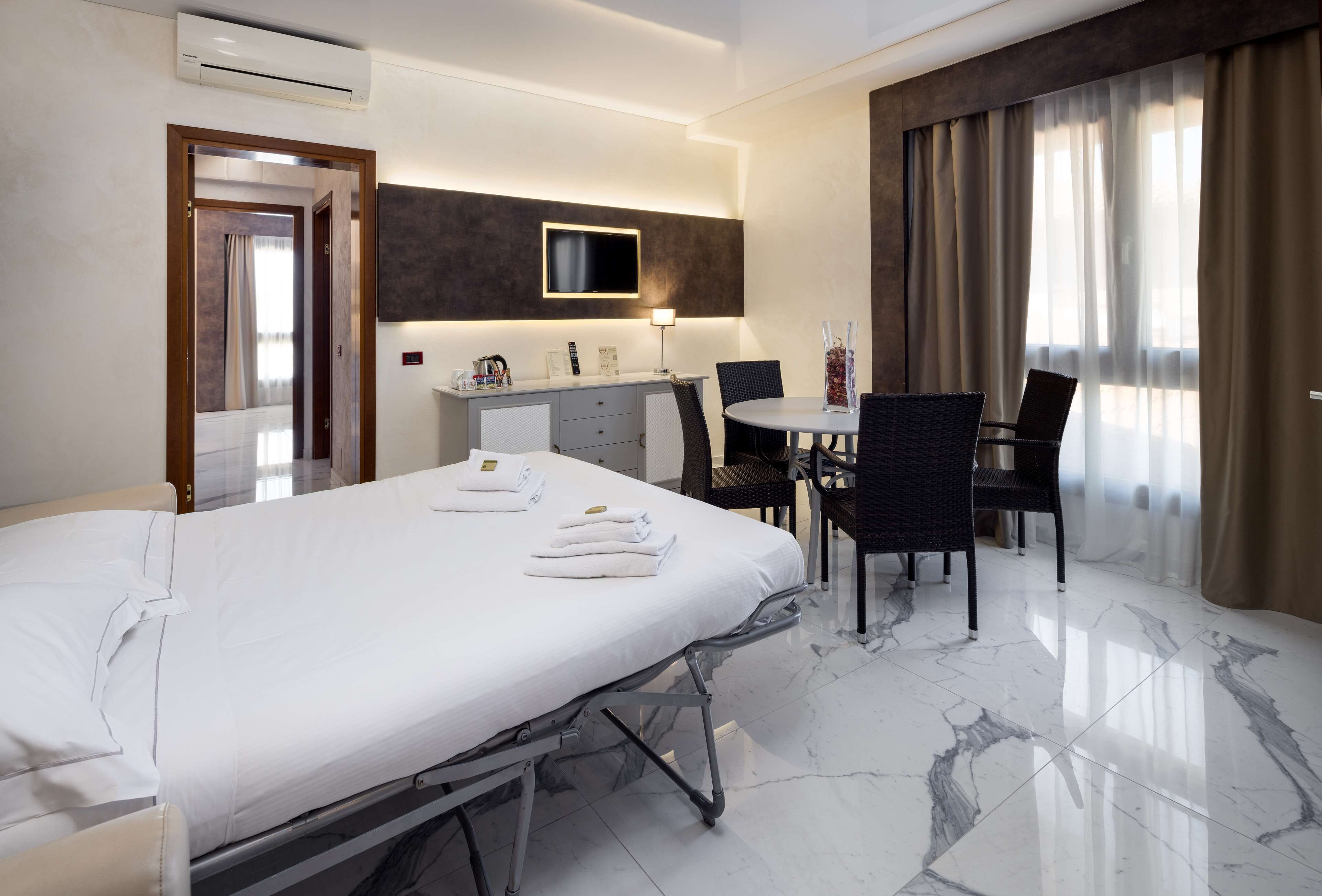 A hotel room with a bed, a desk, a chair, a TV, and a window with curtains.