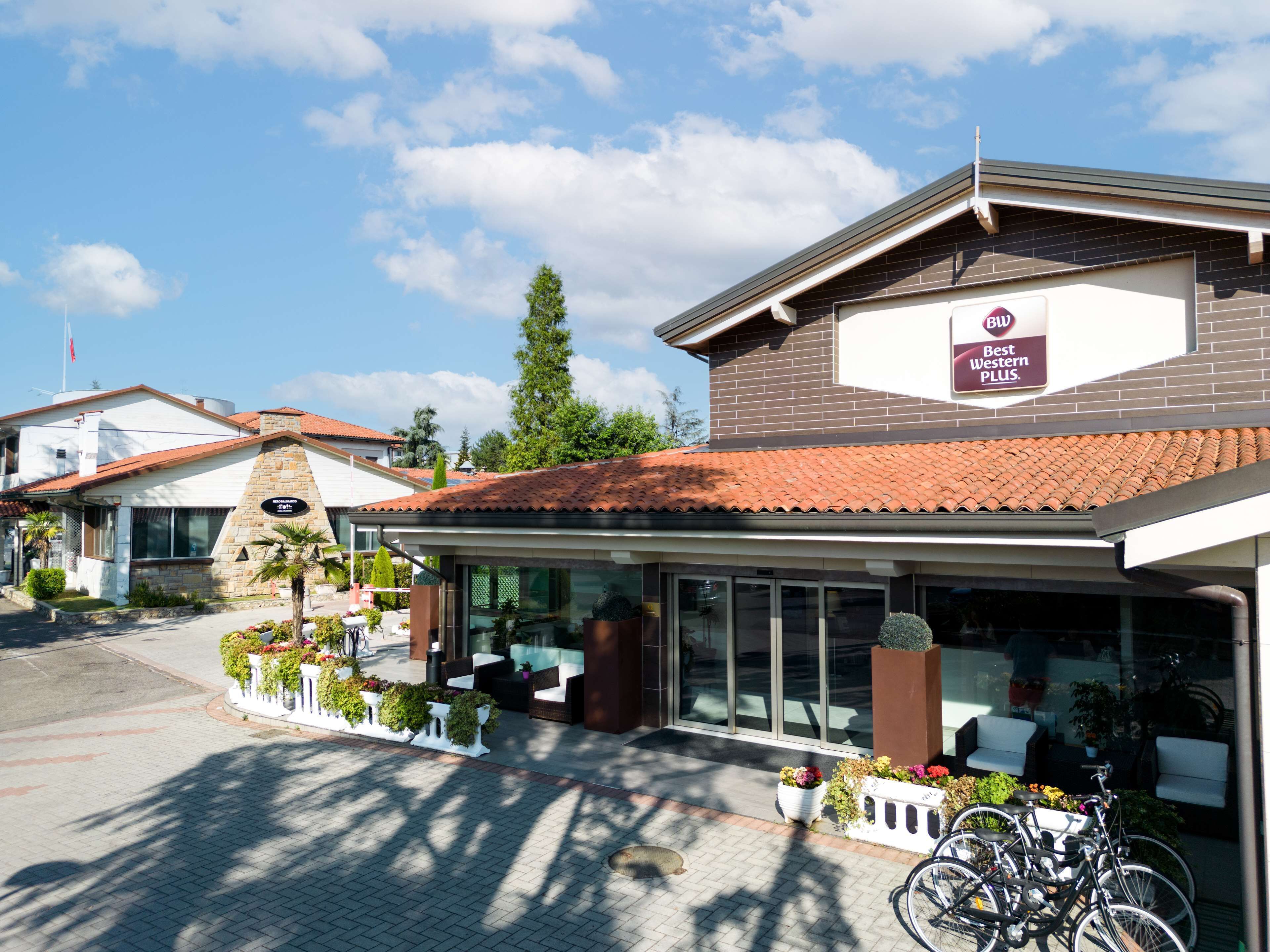 A hotel with a sign reading "Best Western PLUS" and a covered outdoor seating area with potted plants.