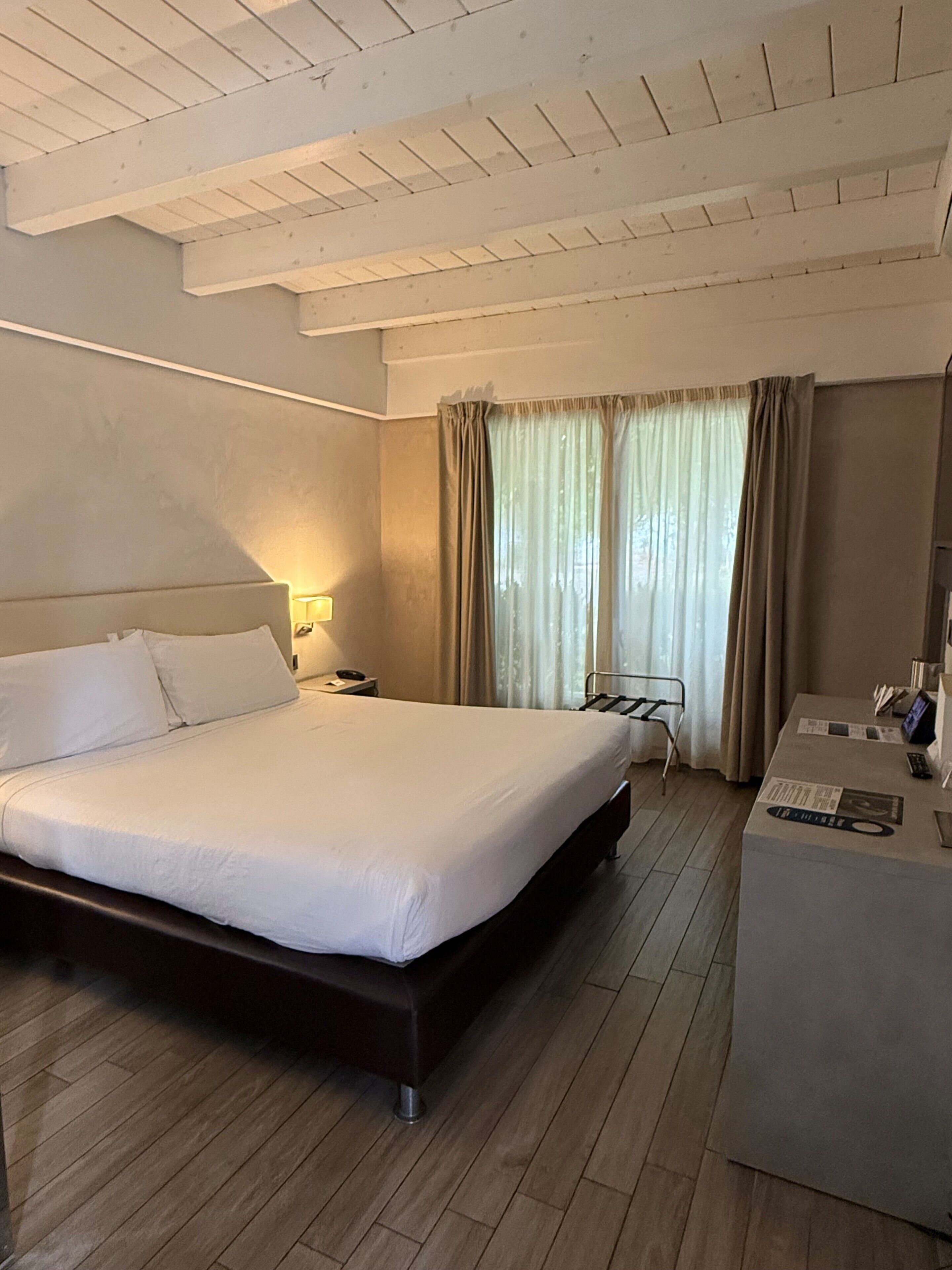 Quarto de hotel com cama grande, mesa de cabeceira, abajur e escrivaninha com cadeira.