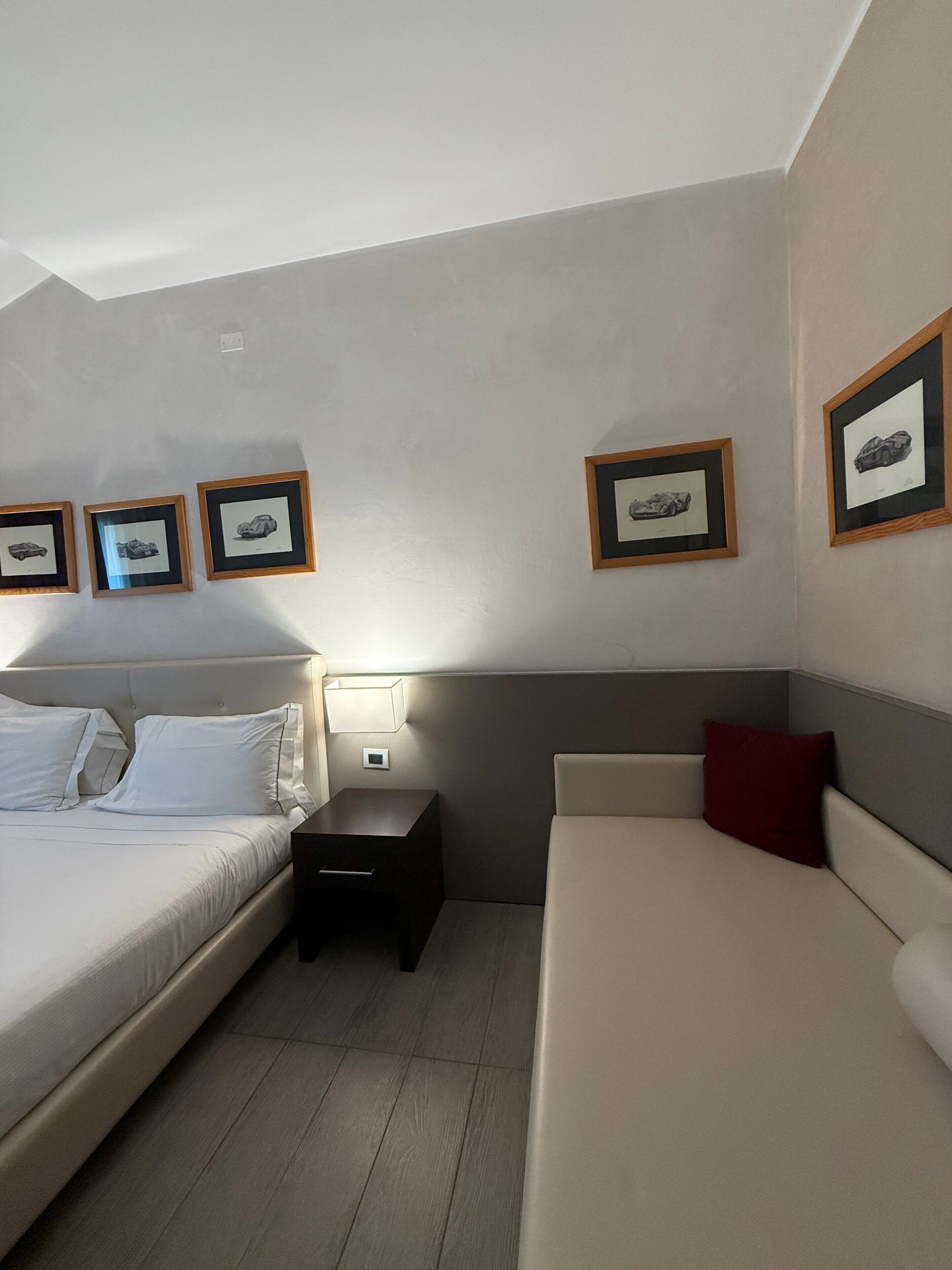 Une chambre d’hôtel avec un lit, une table de chevet, une commode, un canapé et des tableaux encadrés au mur.