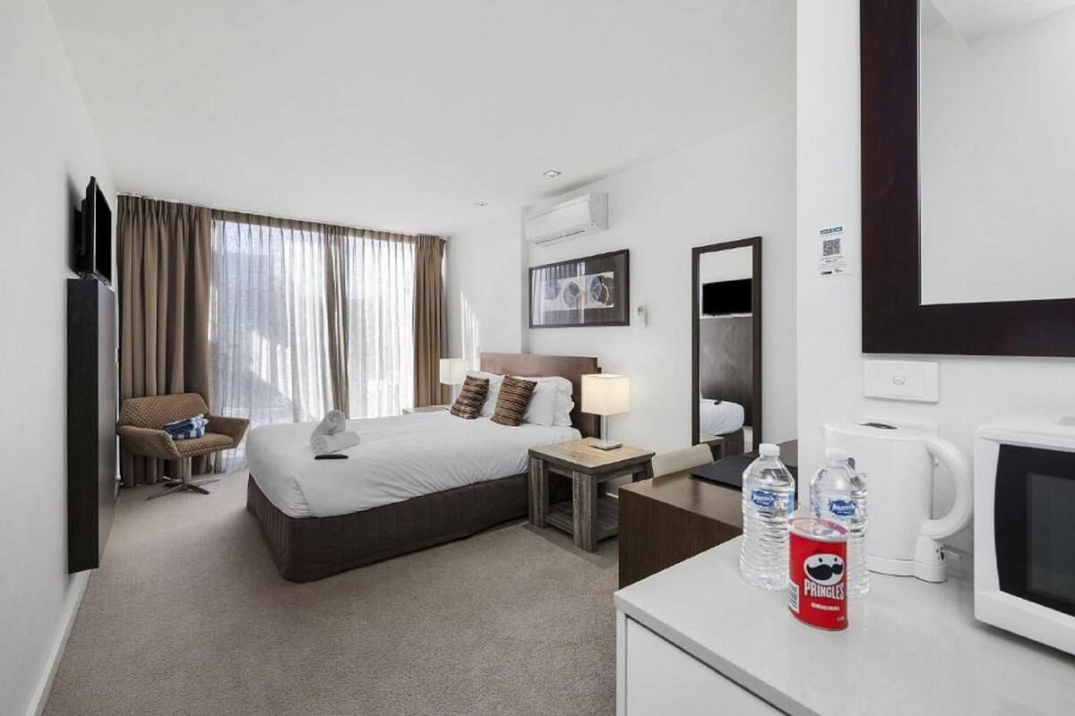 Une chambre d’hôtel équipée d’un lit, d’un bureau, d’une chaise, d’une télévision, d’un miroir et d’une fenêtre avec des rideaux.