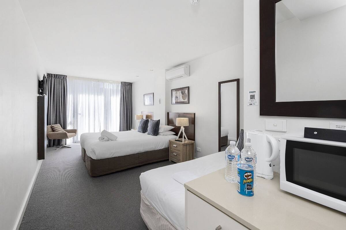 Une chambre d’hôtel avec un grand lit, un bureau équipé d’un micro-ondes, une chaise et une fenêtre avec des rideaux.