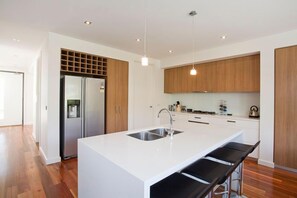 A modern kitchen with a central island, stainless steel appliances, and wooden cabinetry. - Beachfront Resort Torquay (Torquay)