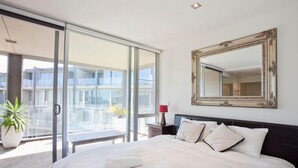 Een moderne slaapkamer met een groot bed, een schuifpui naar een balkon, een grote spiegel en een pot met een plant.