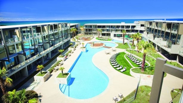 Een resort met een groot zwembad, meerdere gebouwen en uitzicht op de oceaan.