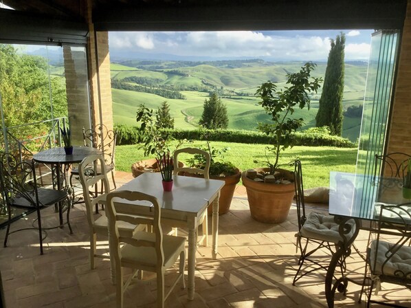 Un patio con mesa y sillas, plantas en macetas y vistas a colinas ondulantes.