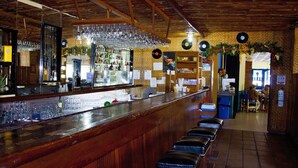 A bar area with a wooden counter, stools, and a mirrored wall. - Hotel Guadaira Resort (Melgar)