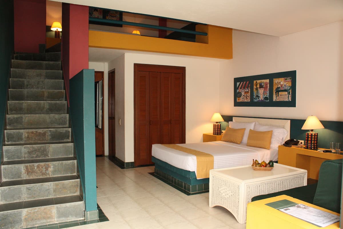 A hotel room with a bed, a desk, a chair, a staircase, and a door.