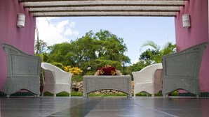 A covered outdoor seating area with wicker chairs and a central planter with flowers. - Hotel Guadaira Resort (Melgar)