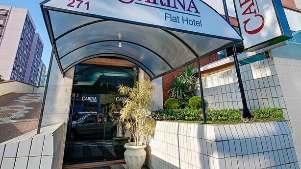 De ingang van Hotel Carina Flat, met een modern ontwerp, een duidelijke entree en een bord met de naam en het adres van het hotel.