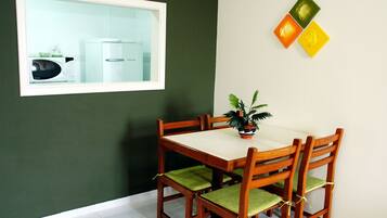 Uma área de refeições com mesa e cadeiras, uma planta em vaso e um micro-ondas visíveis através de uma janela.