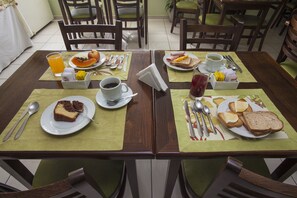A dining table set with plates of food, cutlery, and drinks, surrounded by chairs.