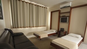 Een hotelkamer met een bank, twee eenpersoonsbedden, een televisie en een airconditioning.