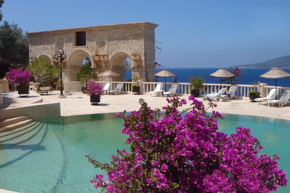 A pool area with a stone building, lounge chairs, and umbrellas.
