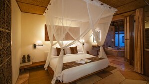 A room with a four-poster bed, a bedside table with a lamp, and a view of the outside through a window.