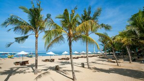 A beach with palm trees, beach chairs, umbrellas, and boats.