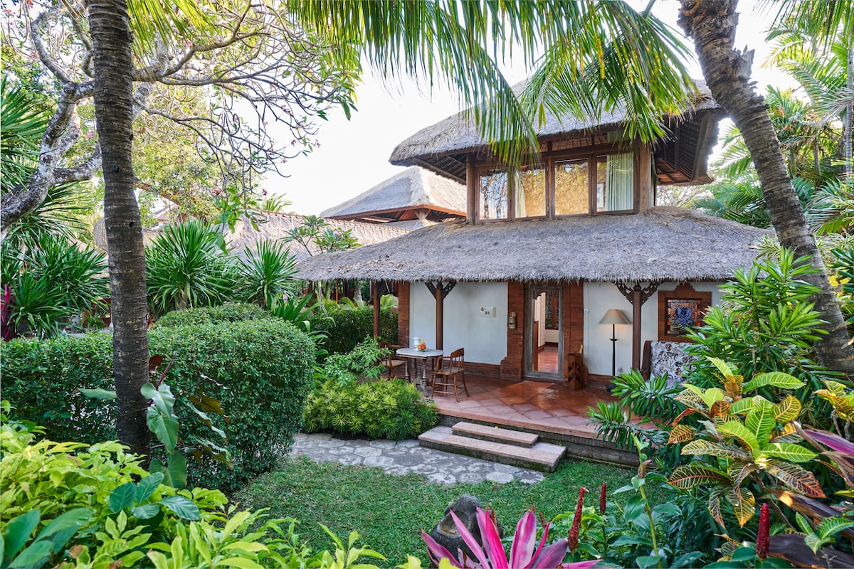 Una casa con techo de paja y un patio, rodeada de exuberante vegetación tropical.