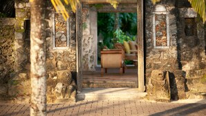 A stone doorway leading to a room with a sofa and a small table, surrounded by lush greenery.