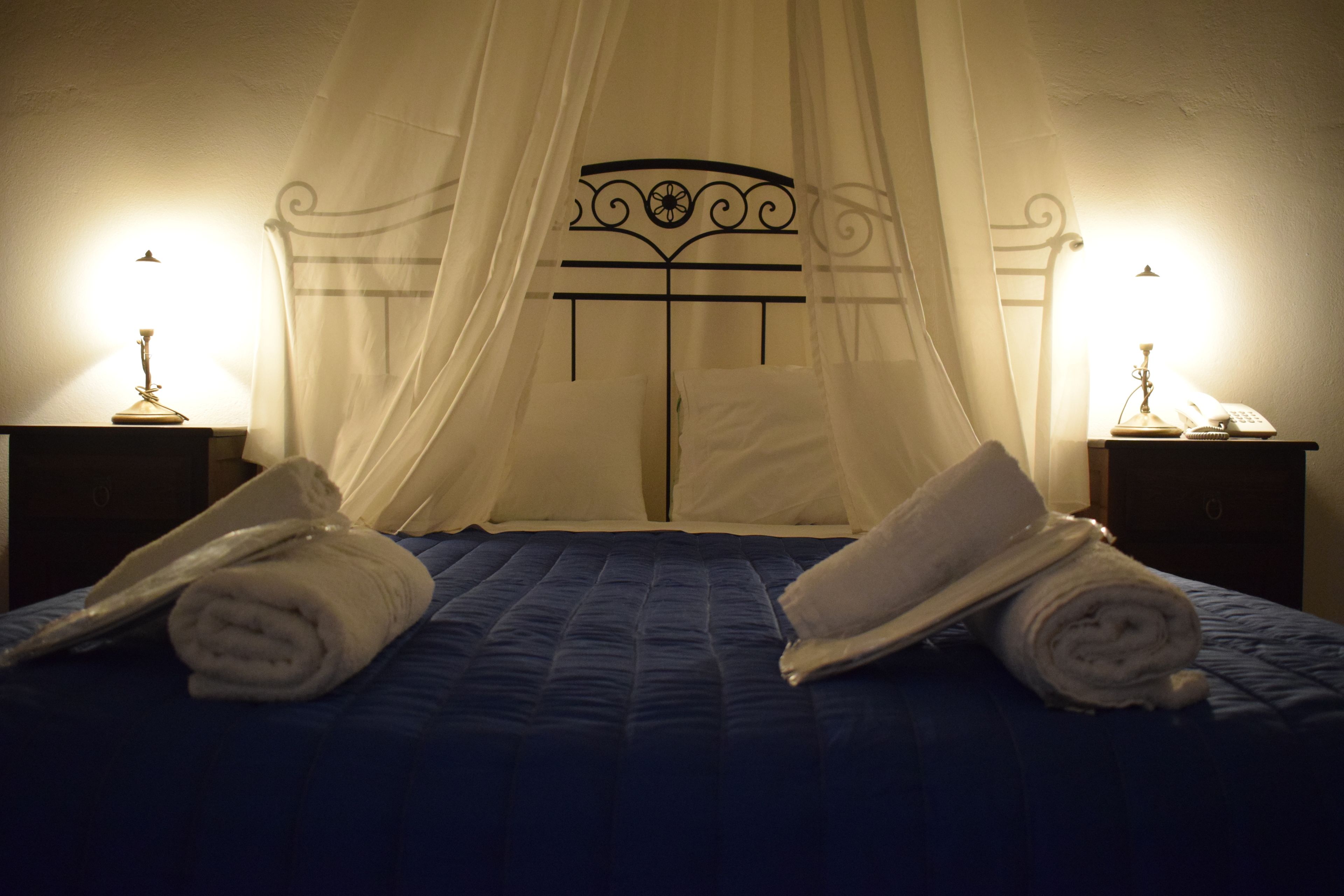 Een bed met hemelbed, twee nachtkastjes met lampen, en opgerolde handdoeken op het bed.