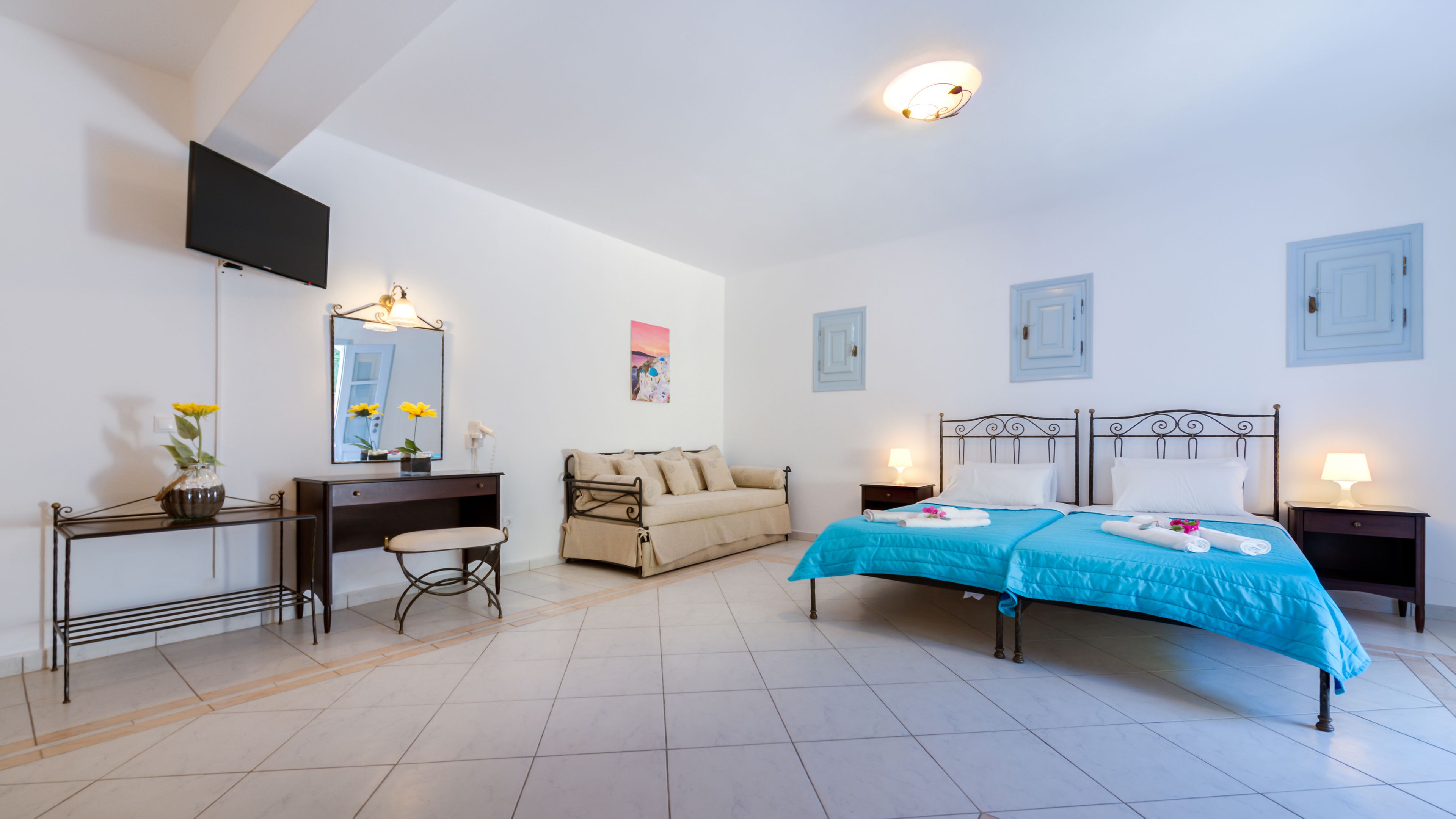 Un dormitorio con cama, mesitas de noche, escritorio, silla, cómoda, espejo y televisor.