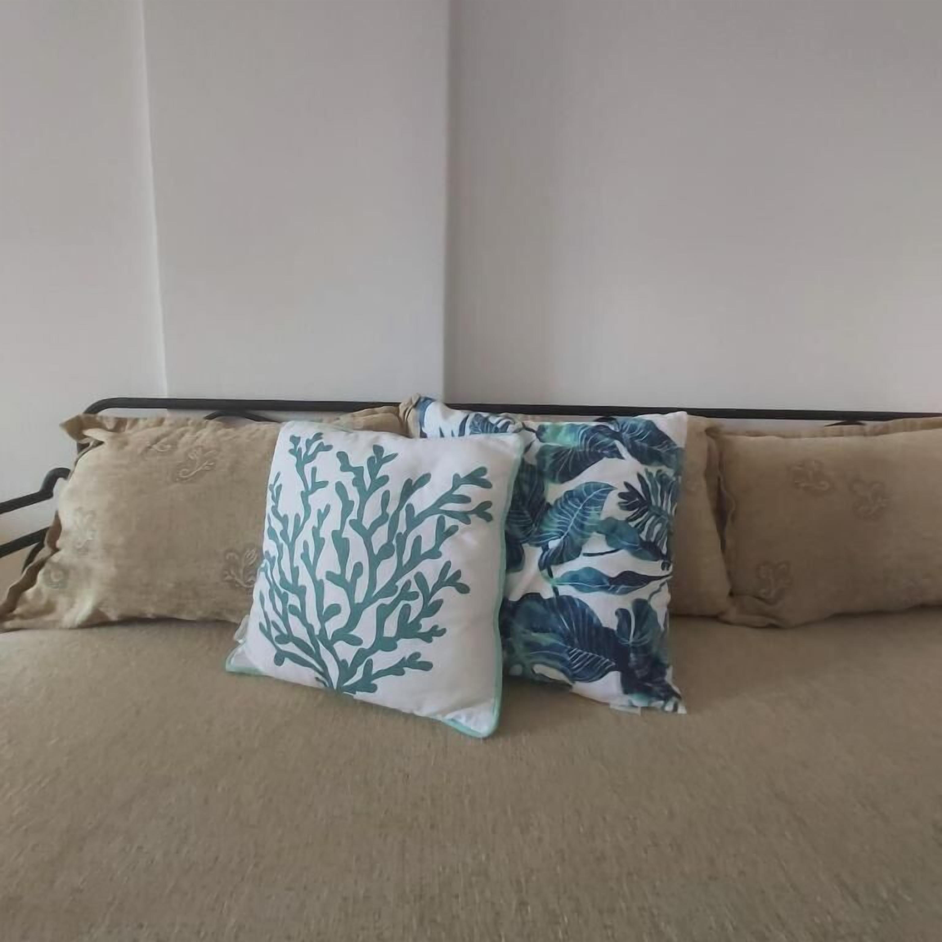 Un lit avec une literie de couleur beige et trois oreillers, dont l’un est orné d’un motif de feuilles.