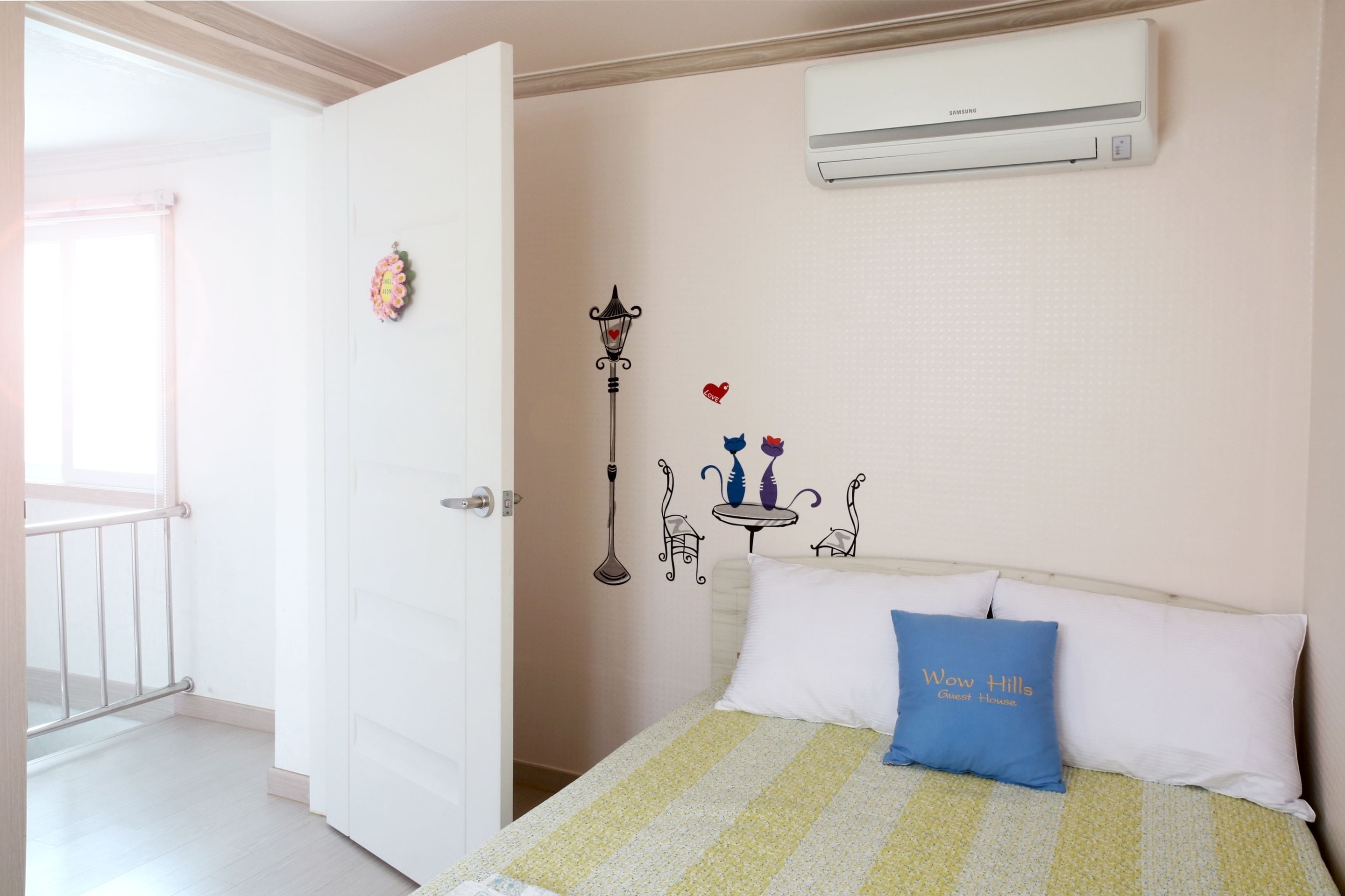 A bedroom with a bed, a nightstand, a wall-mounted air conditioner, and a window with a view.