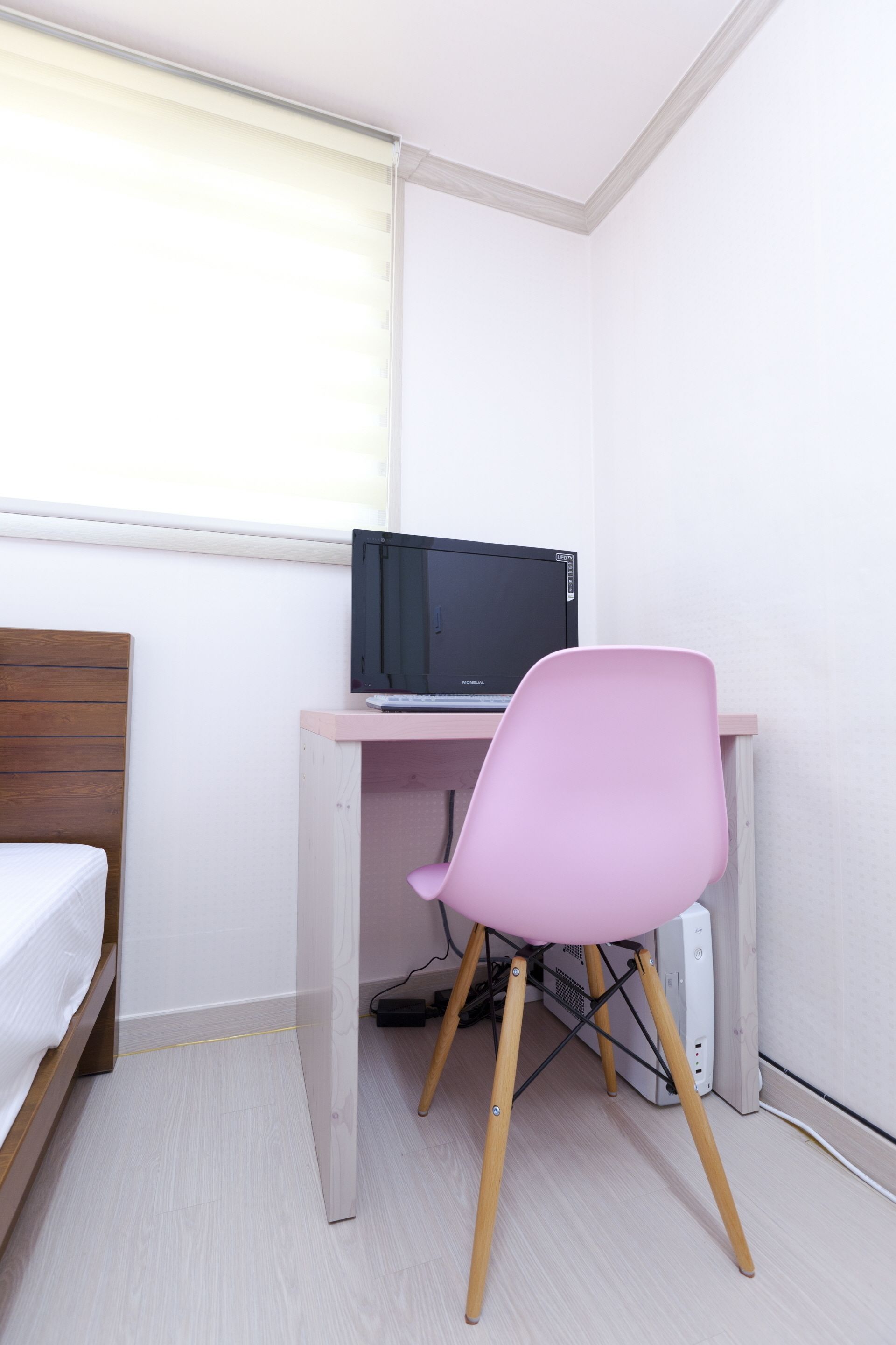 Une petite pièce, bien rangée, avec un lit, un bureau doté d’un ordinateur et une chaise rose.