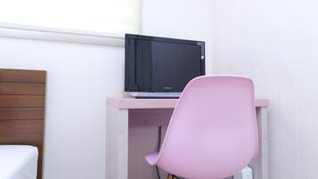 Une petite pièce, bien rangée, avec un lit, un bureau doté d’un ordinateur et une chaise rose.