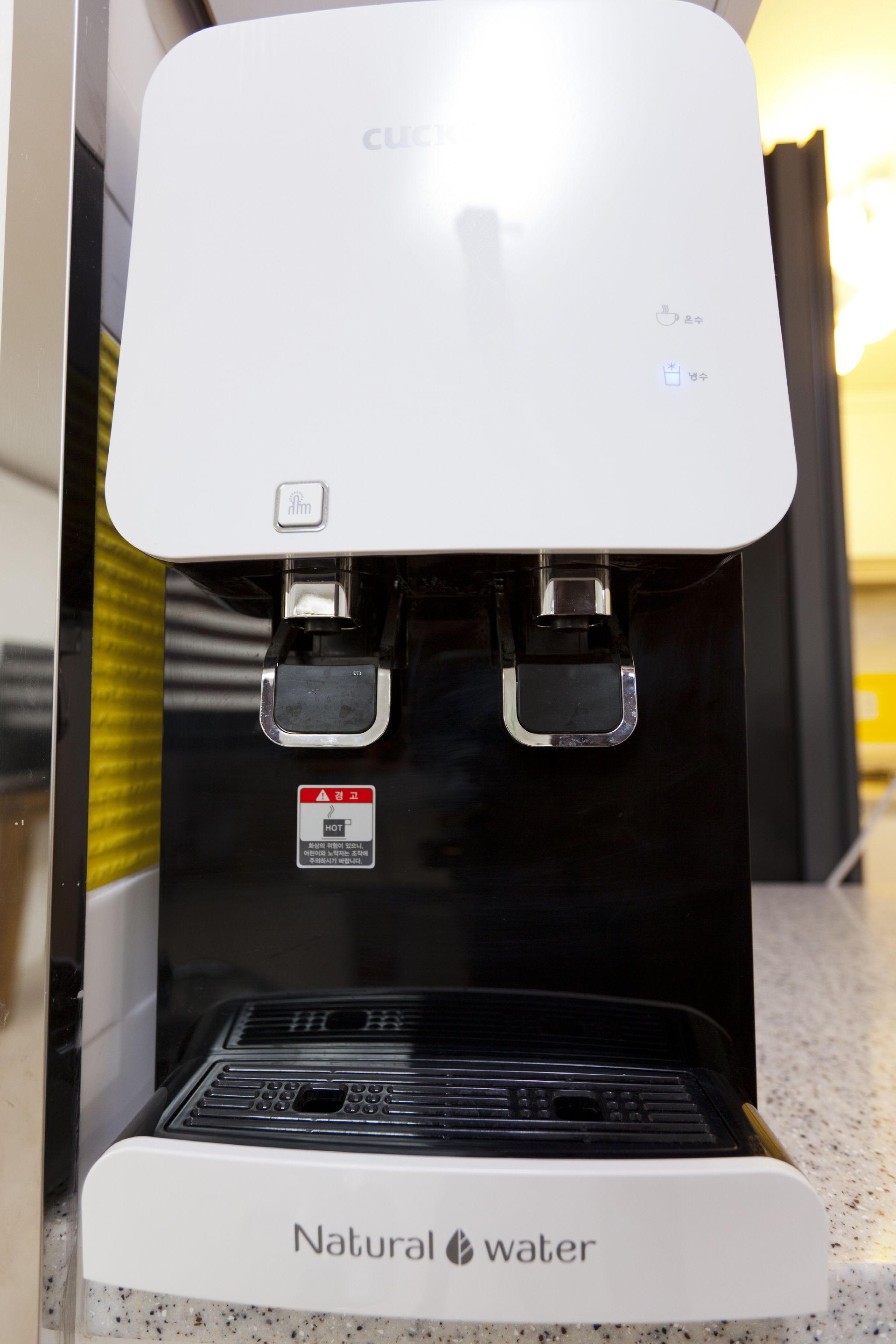 Dispensador de agua con etiqueta que dice "Natural Water", indicador de agua caliente y panel de control con botón de encendido.