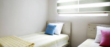 Un dormitorio con dos camas individuales, cada una con almohada y manta. Hay una ventana con persianas, un equipo de aire acondicionado en la pared y un cabecero de madera.