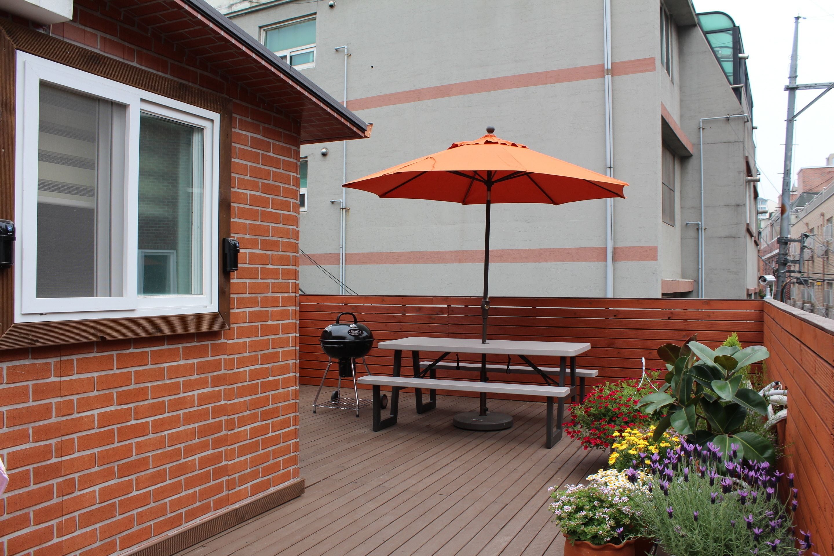 Un patio con una mesa y banco de madera, una parrilla y un paraguas naranja.