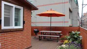 Un patio con una mesa y banco de madera, una parrilla y un paraguas naranja.