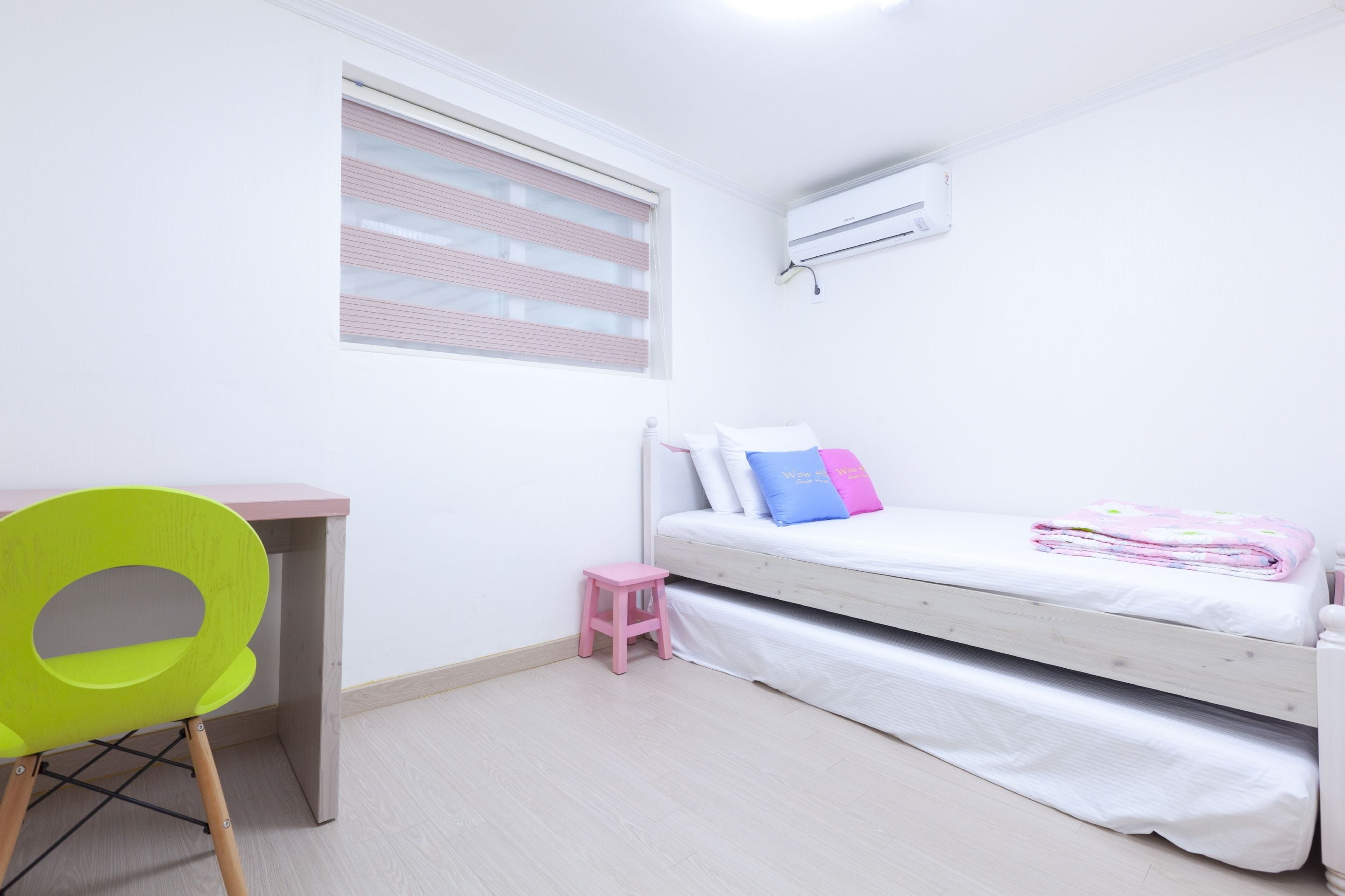 A bedroom with a bed, a desk, a chair, and a window with blinds.