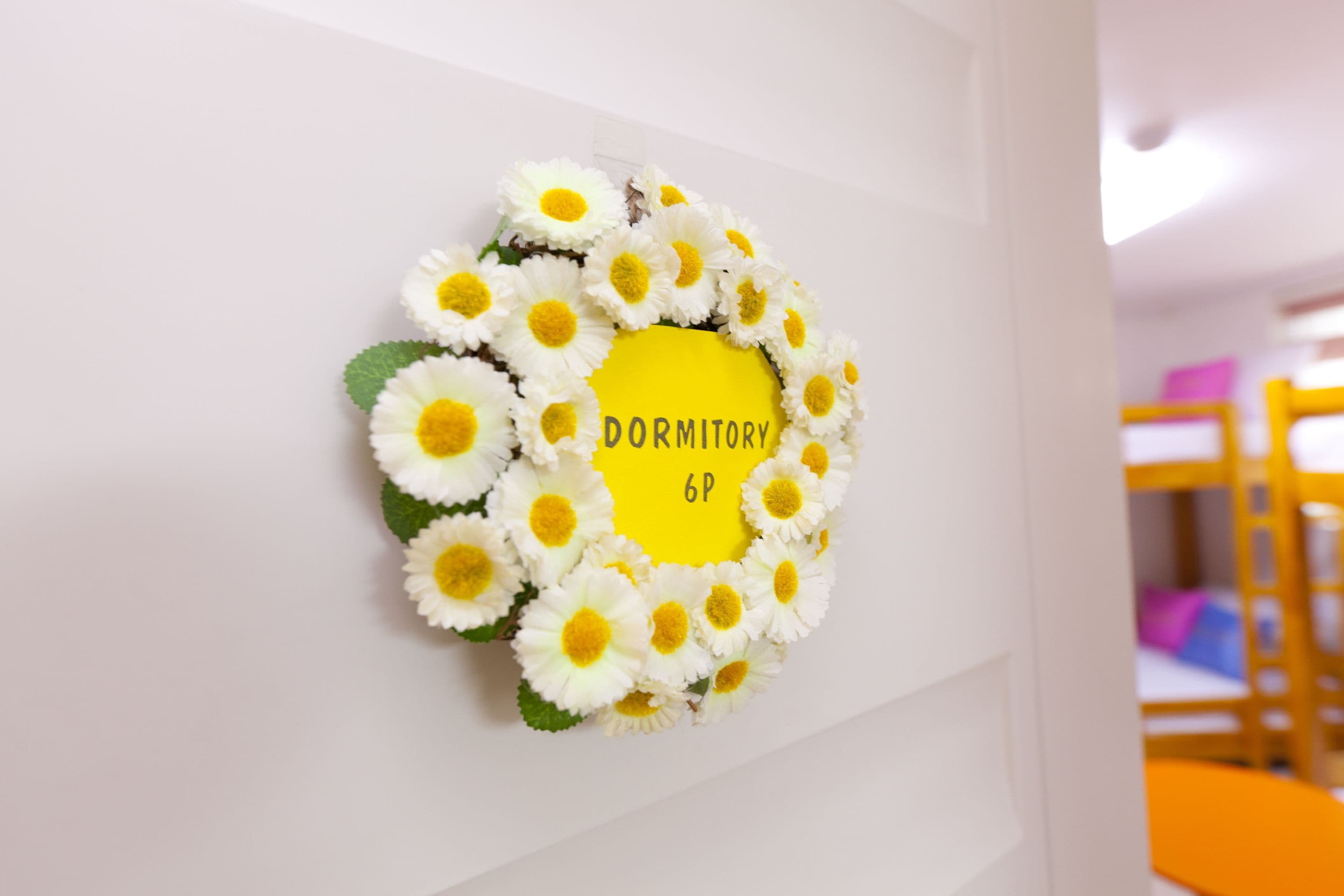 A wall decoration with a circular arrangement of white flowers and a yellow sign that reads "DORMITORY 6P".