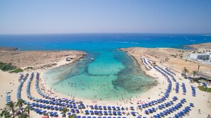 Na praia, areia branca, espreguiçadeiras, guarda-sóis