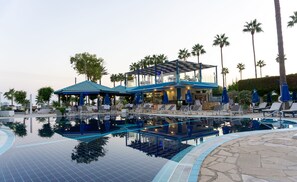 Un espace piscine avec des chaises longues et des parasols, un bar et un bâtiment doté d’un toit bleu.