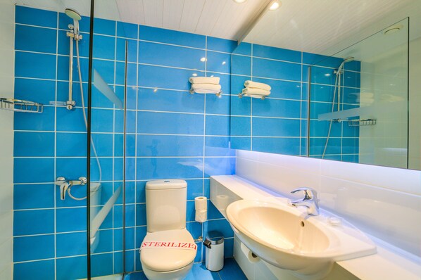 A bathroom with blue tiled walls, a toilet, a sink, and a glass shower enclosure.