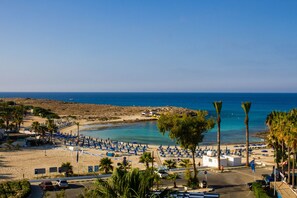 Une plage avec une eau d’un bleu limpide, des palmiers et des parasols.