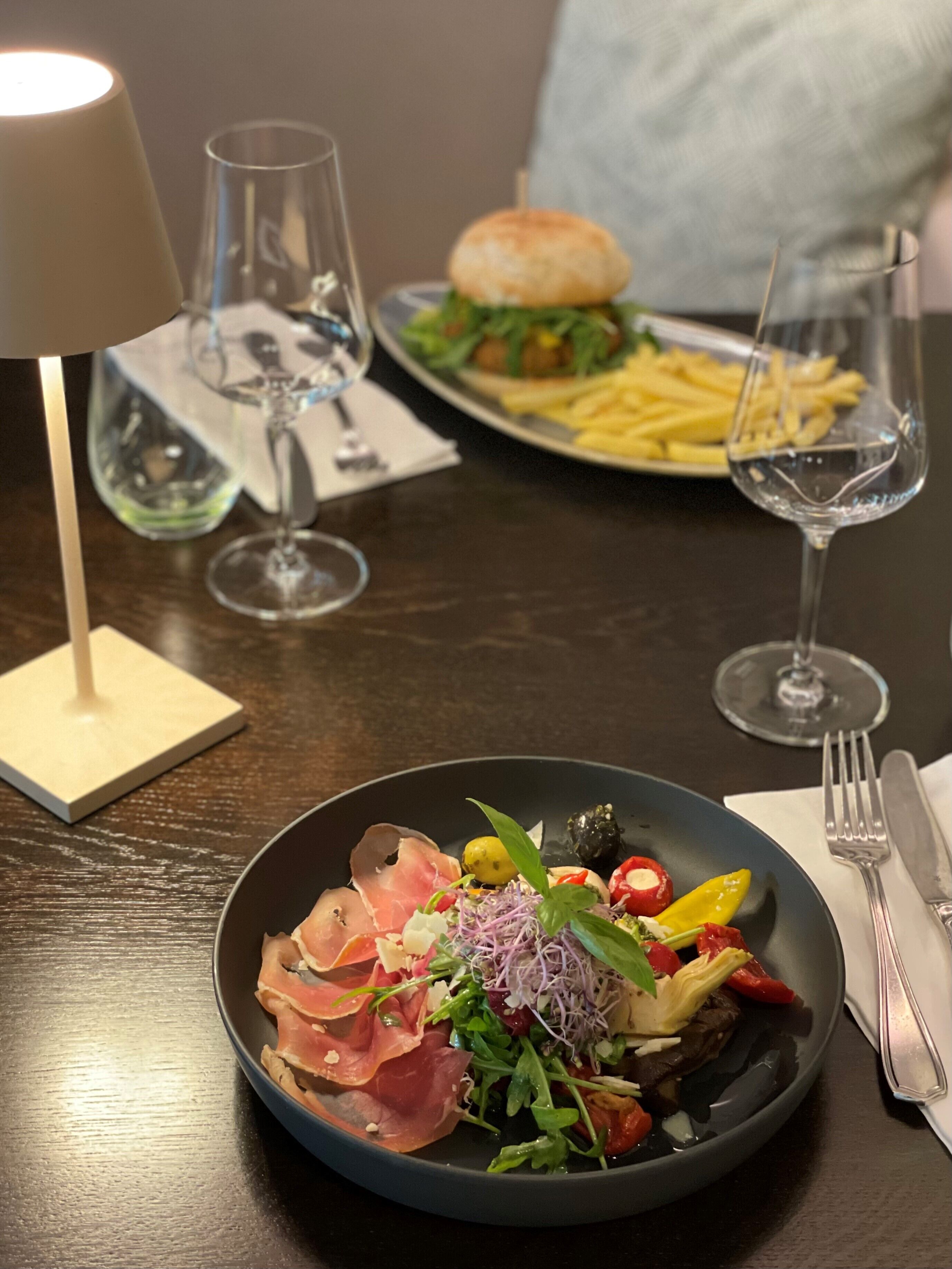A dining table with a plate of food, a glass of water, and a lamp.