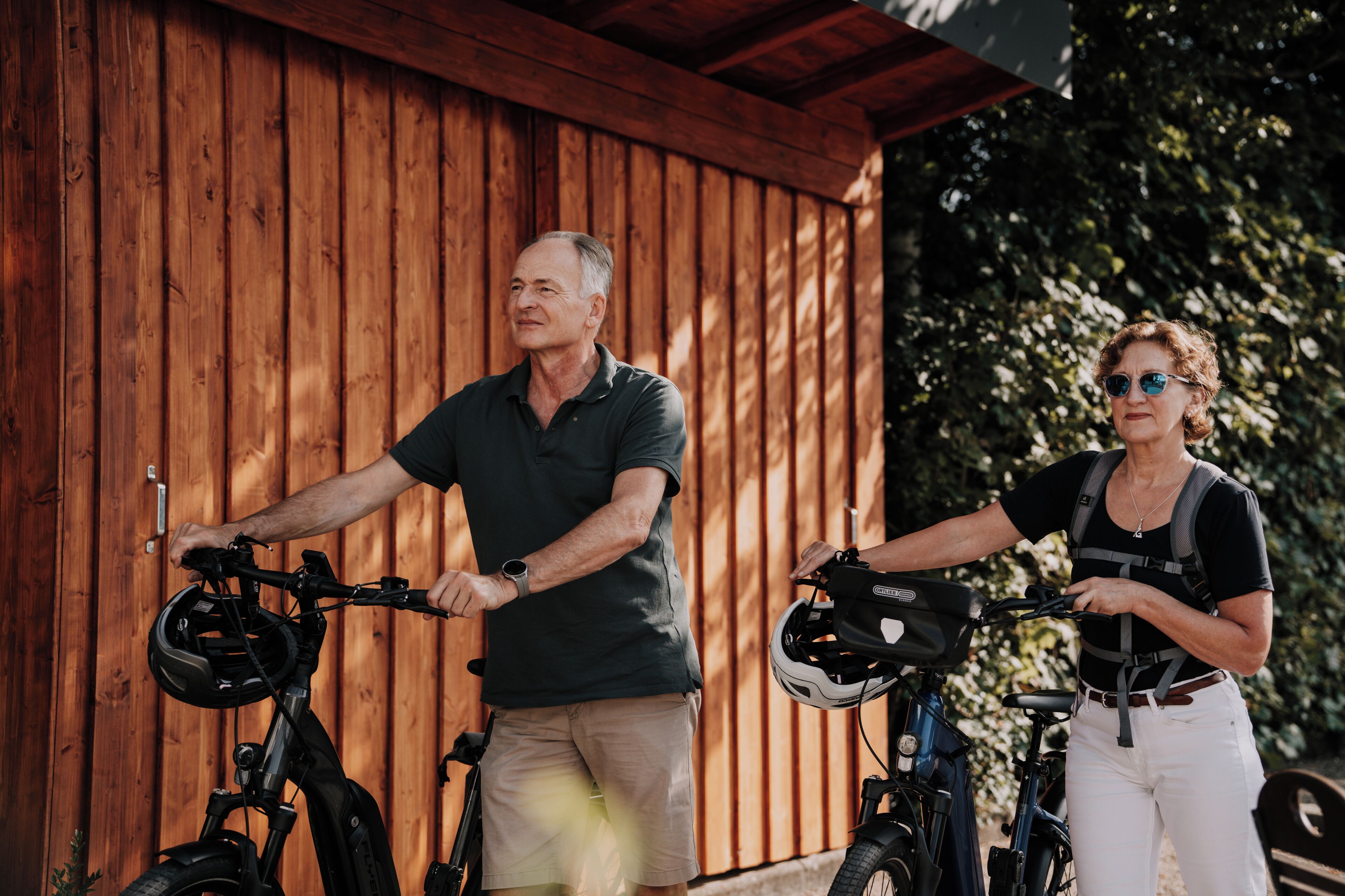 Twee mensen op elektrische fietsen voor een houten gebouw.
