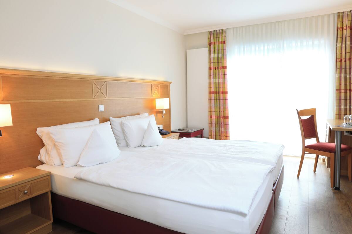 A hotel room with a large bed, bedside tables, a desk, and a chair.